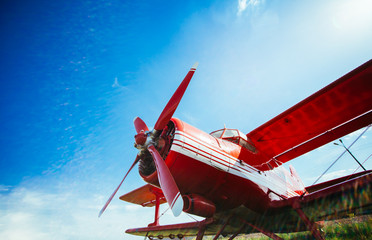 Red retro airplane stands on grass against a blue sky with flare