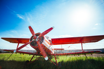 Naklejka premium Czerwony samolot retro stoi na trawie przeciw błękitne niebo z flary