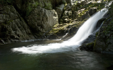 cascatella  che si getta in un laghetto lungo il torrente alpino. 
