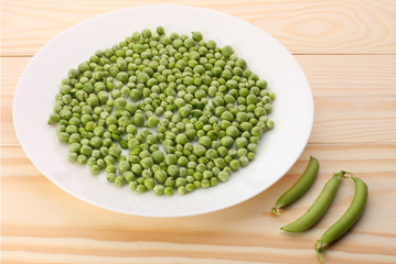 Green peas  in white plate and pea pods  on wooden table