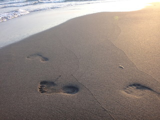 Fototapeta na wymiar Следы на песке на пляже вечером в закатном солнце и с набегающей волной