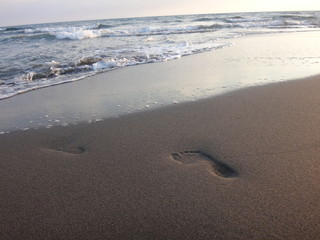 Следы на песке на пляже вечером в закатном солнце и с набегающей волной