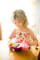 Little girl eating corn balls in the kitchen. Morning light