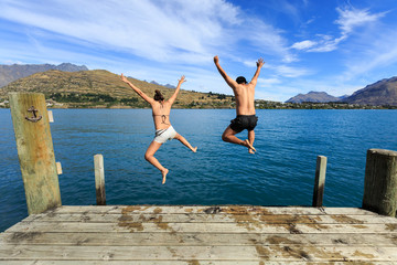 Young couple jumping on the edge of a dock in to the lake - 86171860