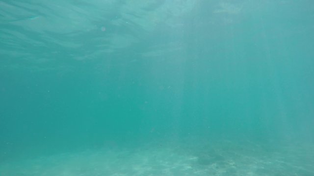 Calm sea surface in slow-motion from underwater with sun rays going through.