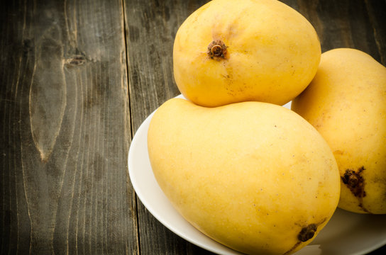 Ripe mango,tropical fruit on white plate and wooden background