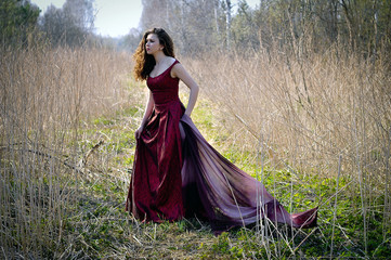 Fototapeta premium Portrait of woman in long red dress hiding in the forest