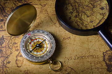 Fototapeta na wymiar Compass and magnifying glass on old map