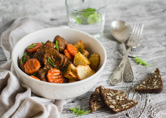 beef goulash with carrots and roasted potatoes in a white bowl on a light wooden background