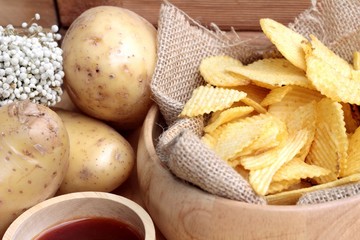 Potato chip and fresh potatoes on wood background