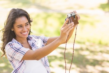 Pretty brunette taking a selfie with retro camera in the park