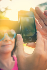 Mid adult woman with heart shaped sunglasses and hat taking selfie with smart phone