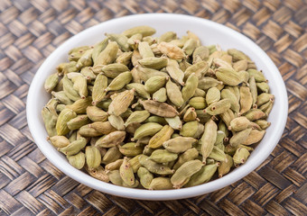 Cardamom spices in white bowl over wicker background