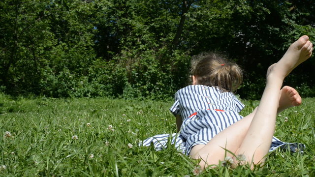 Little girl lying on green grass in the park.