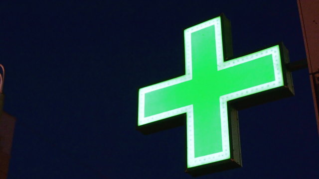 Green flashing neon pharmacy cross against a night sky providing a bright symbol of healthcare
