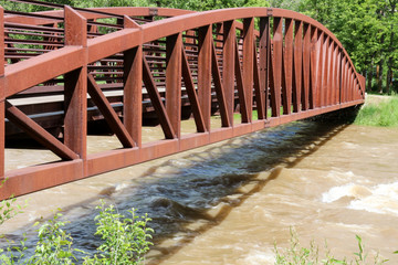 Brown pedestrian bridge crossing the brown, swollen Animas River in Durango, Colorado