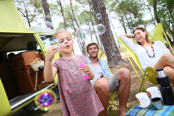 Little girl blowing soap bubbles, parents in background