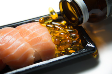 Fototapeta na wymiar Fish oil pills poured and served with sushi salmon isolated