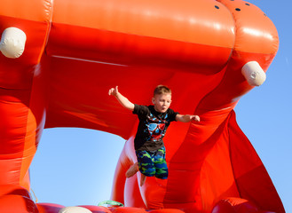 Blonde boy jumping in air on red bouncy castle