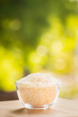 Polished rice heap in glass bowl with green nature background.