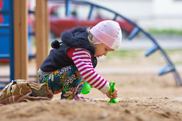 Litle girl playing with sand in sandbox