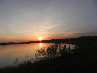 Яркий закат с красными и рыжими оттенками над озером летом