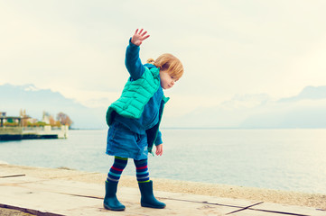 Outdoor portrait of adorable toddler girl of 2 years old, wearing green waistcoat, denim skirt and...
