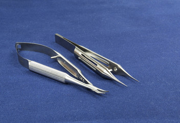 Two microsurgical instruments on blue background