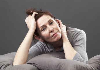 tired senior woman resting her face and hands laying down on cushions for comfort and relaxation