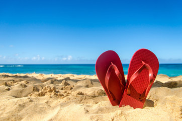 Fototapeta na wymiar Red flip flops in heart shape on the sandy beach