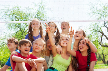 Teenagers sitting under volleyball net pointing