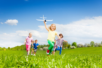 Girl with airplane toy runs fast and kids behind