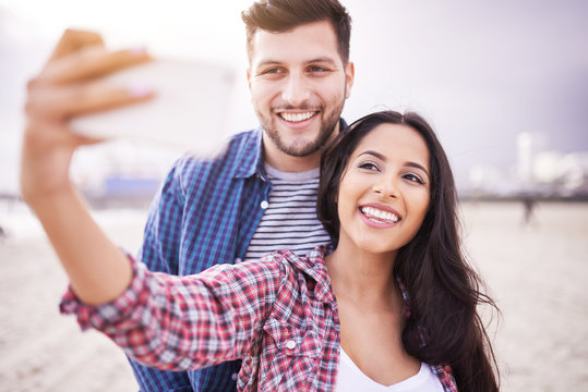 happy couple taking selfie on beach with smartphone