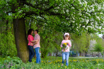 Obraz na płótnie Canvas a girl collects the field flowers in a bouquet sits near parents