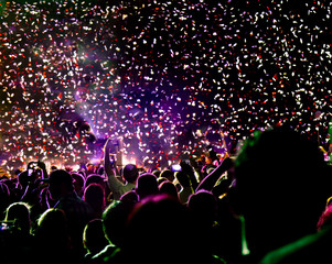 Music fans cheering in a shower of confetti at the end of a concert.
