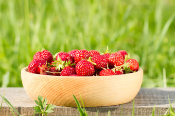 fresh ripe strawberries in a wooden bowl on a green meadow