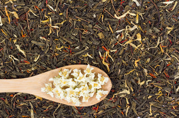 wooden spoon with dried jasmine flowers on a background of tea. View from above.