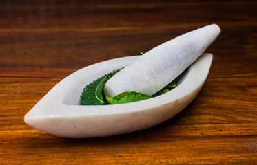 A marble pestle and mortar with neem leaves on a wooden surface.