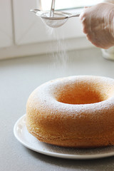 Frau streut Puderzucker über Kuchen in der Küche