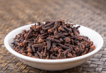 Clove spices in a white bowl on wicker background