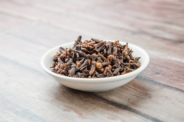 Clove spices in white bowl over weathered wooden background