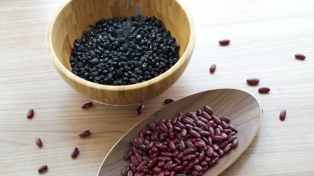 red and black beans pouring to fill wooden bowl