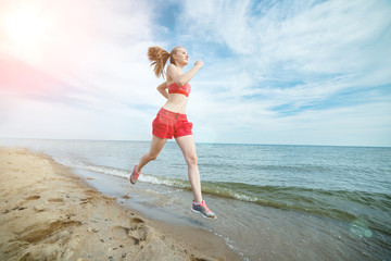 Naklejka premium Young lady running at the sunny summer sand beach. Workout. Jog
