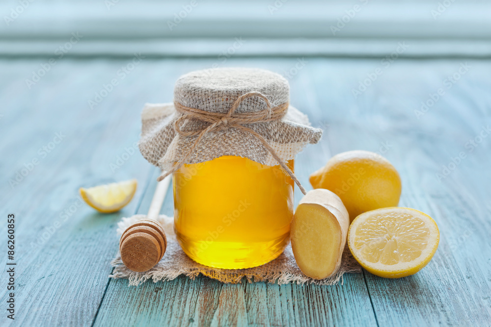 Wall mural Natural honey in a pot or jar with twine tied in a bow, honey dipper, lemon and ginger on a blue wooden background