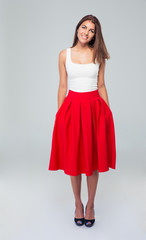 Full length portrait of attractive smiling woman in skirt posing over gray background and looking at camera