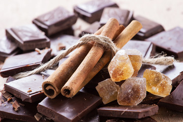Chocolate with cinnamon sticks and piece of brown sugar on coffee background, selective focus