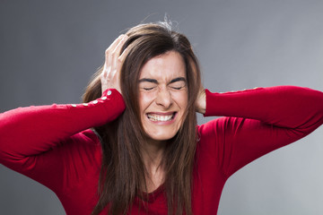 frustrated young woman having painful migraine, covering closed ears and eyes, annoyed by loud...