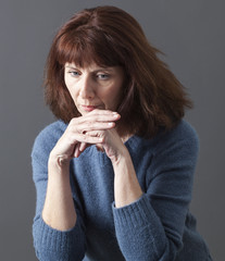 sad 50's woman alone with chin resting on hands for reflection, sadness or fatigue due to menopause