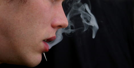 A man with a piercing blowing cigarette smoke out his mouth