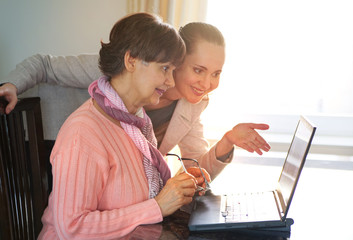 Younger woman helping an elderly person using laptop computer